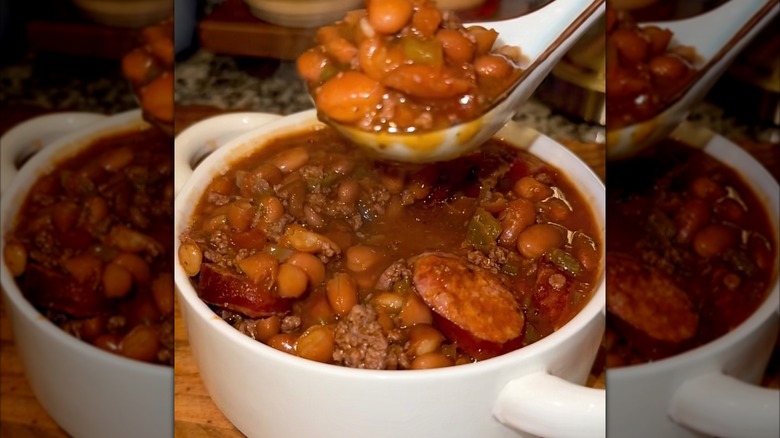A bowl of fireman beans with a reddish brown sauce and evident appearances of sausage, beans, and green chiles