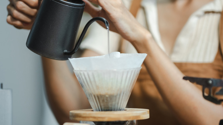 A person pouring hot water over coffee grounds in a filter set inside a dripper cone.