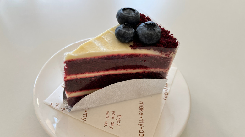 A slice of mahogany cake, frosted and topped with blueberries.