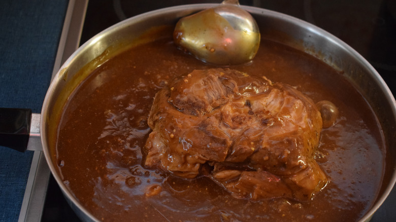 Finished Sauerbraten in a deep pan with sauce and a ladle