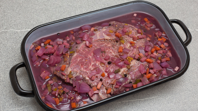 Sauerbraten raw meat and marinade in a rectangular baking dish with black trim