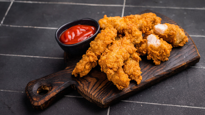 Chicken tenders with bowl of hot sauce on wooden board