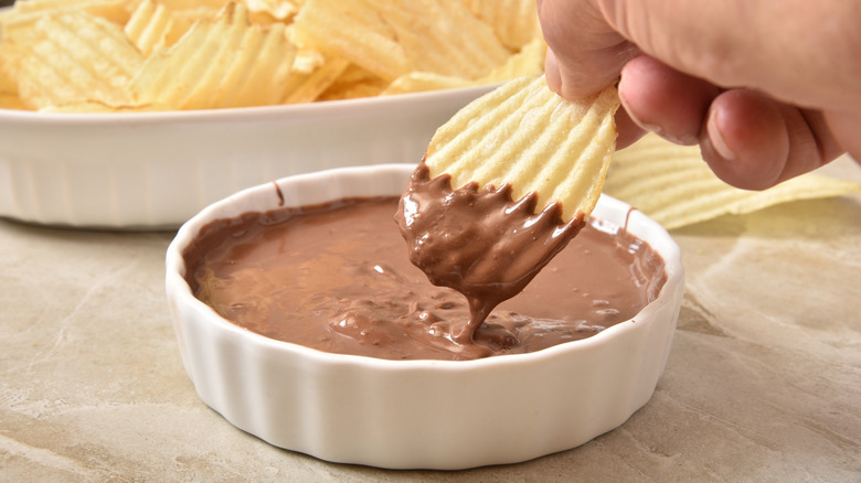 Potato chip being dipped in a bowl of chocolate