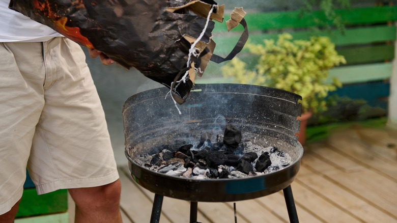 Person emptying bag of charcoal into grill base on residential back deck.