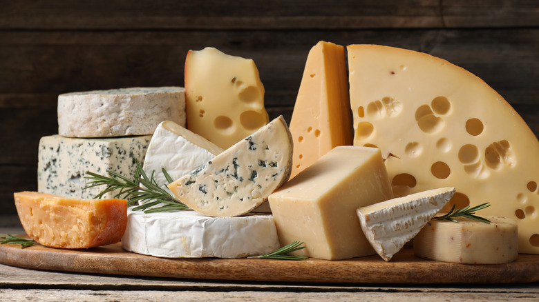 Various cheeses sliced next to each other with fresh rosemary on wood board.