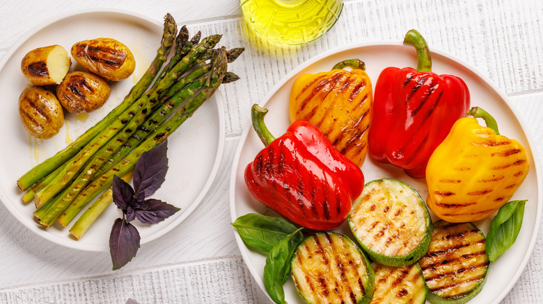 A range of various grilled vegetables on white plates atop white table.