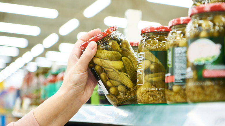 Person grabbing jar of pickles off the shelf at the grocery store.