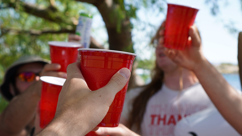 A group of friends all holding red solo cups outstretched in a "cheers" movement.