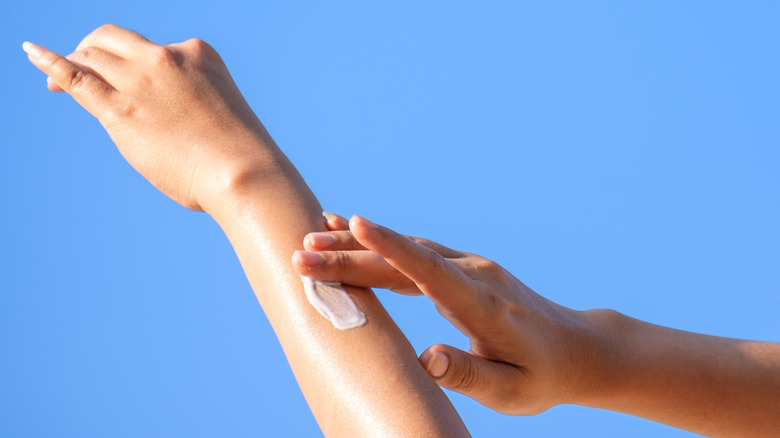 Person applying sunscreen against blue sky.