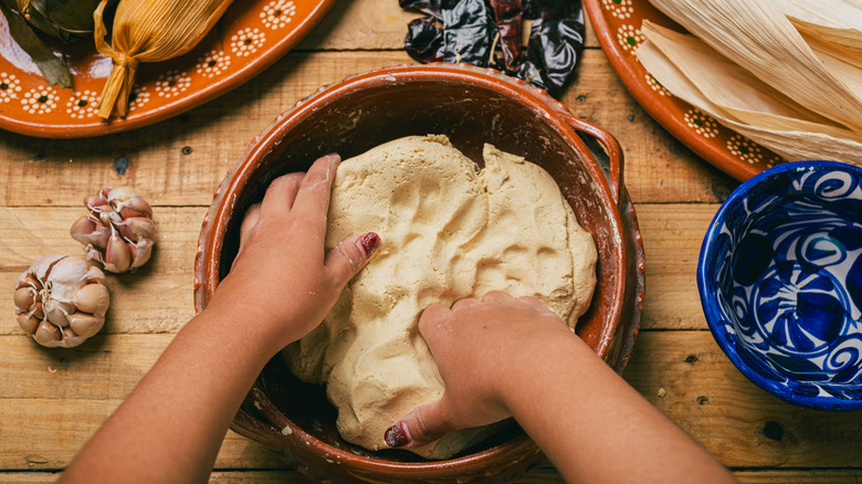 Someone mixing dough for homemade tamales in a brown bowl