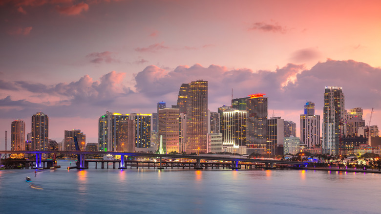 Miami skyline at dusk with building and street lights on in front of a pinkish sunset