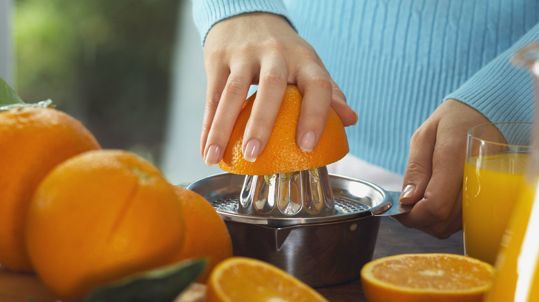 A hand juicing an orange using a reamer juicer, with fresh orange juice in a glass on the side