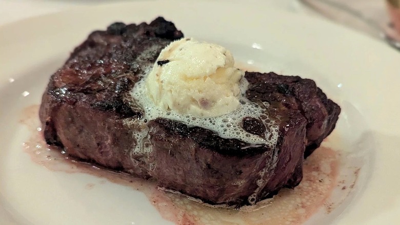 A seared filet mignon topped with butter, served on a white plate