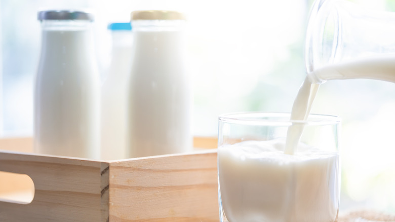 Milk being poured into a glass with three full bottles in a wooden cart behind it