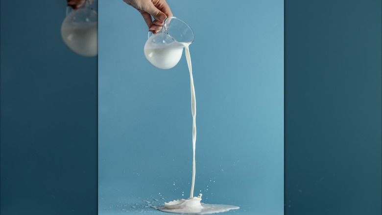 A hand pouring a glass jug of milk onto a flat surface