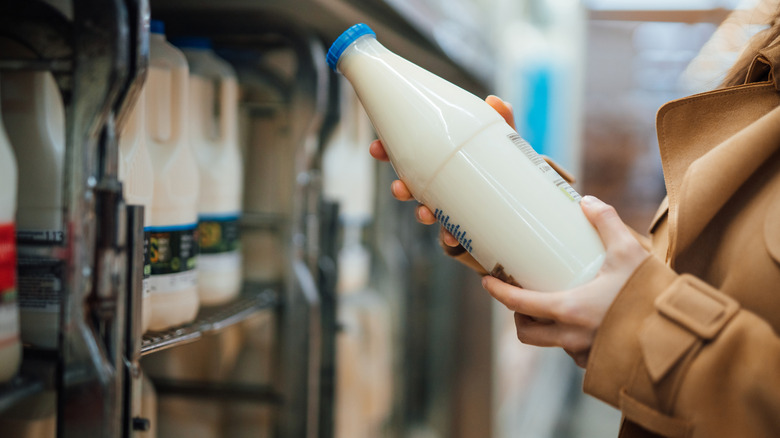 A woman in a trenchcoat holding a glass bottle of milk