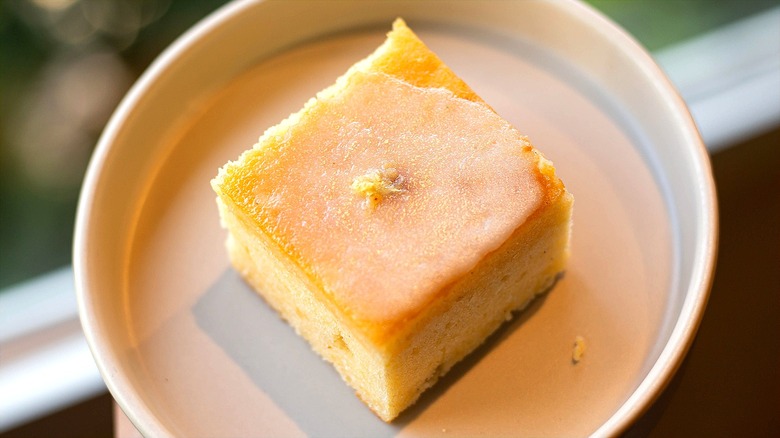 Square slice of vanilla cake with citrus glaze on a white plate