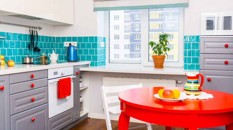 A bright kitchen with a red table and blue backsplash