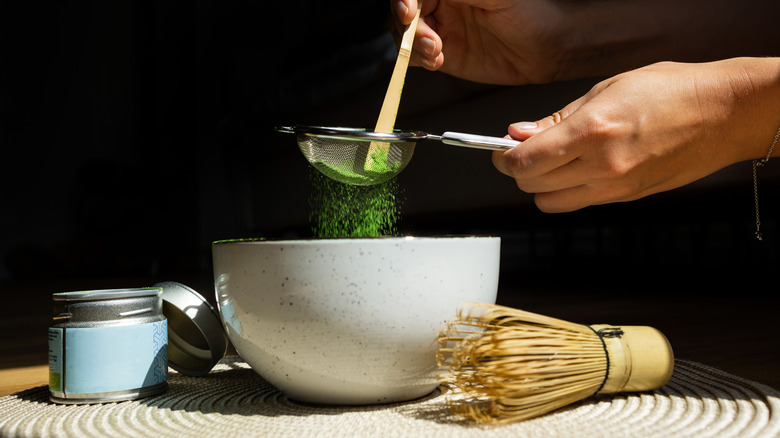 Hands sift matcha powder through a sieve