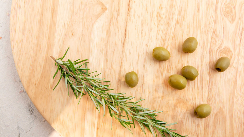 several olives and rosemary sprig on wooden board