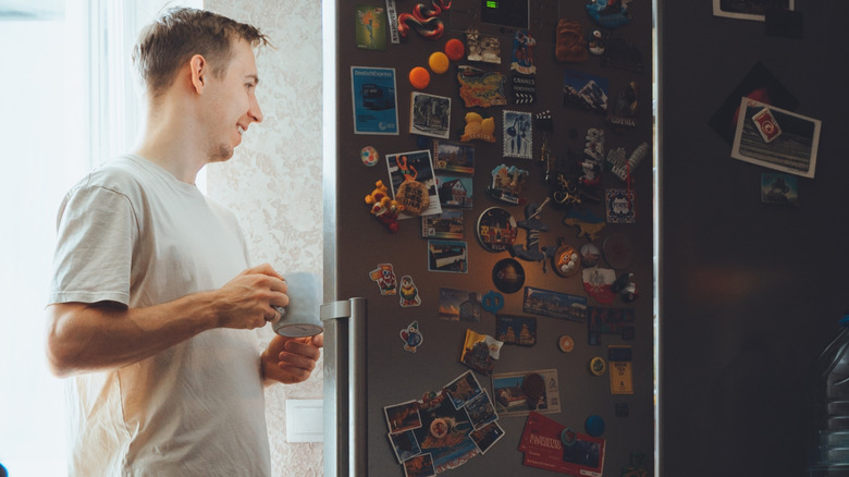 a man holding a mug standing at an open fridge