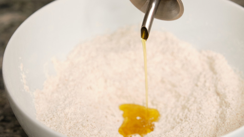 Someone pouring olive oil into a bowl of flour