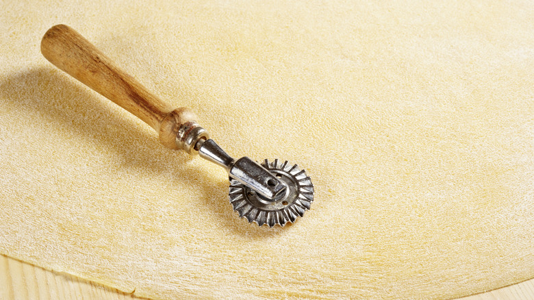 A wooden pasta tool resting on a sheet of freshly rolled out pasta