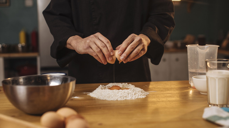 A chef adding an egg to pile of flour to make a pasta dough