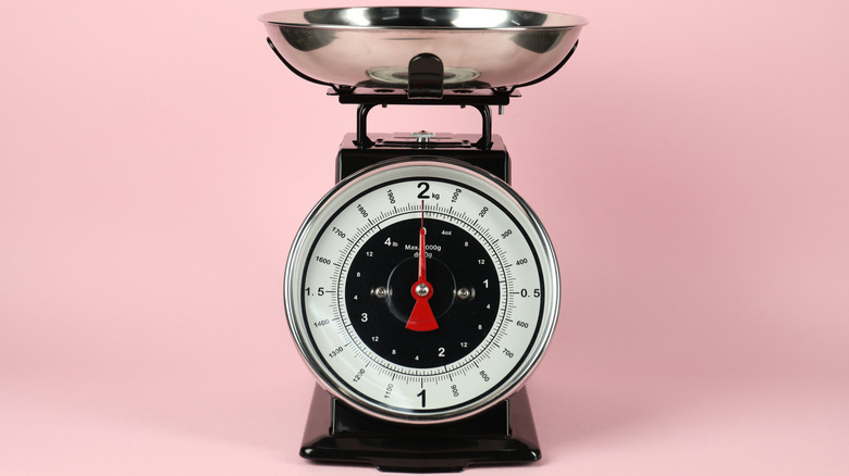A vintage kitchen scale on a pink background