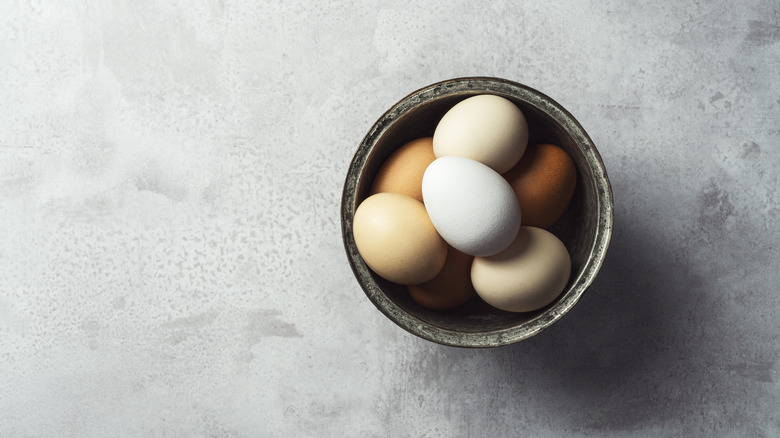 A bowl of various colored eggs on marble countertop