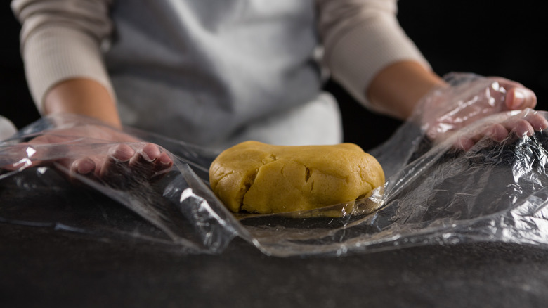 A chef wrapping up dough in plastic wrap