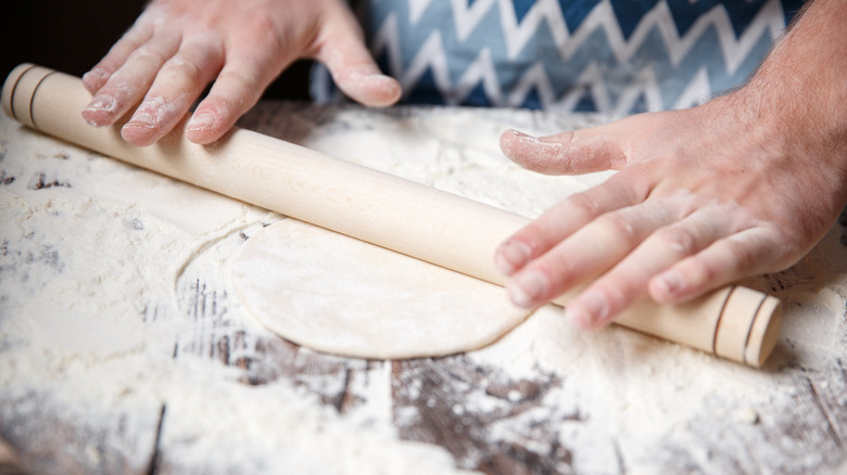 A chef rolling out dough with rolling pin on a floured surface