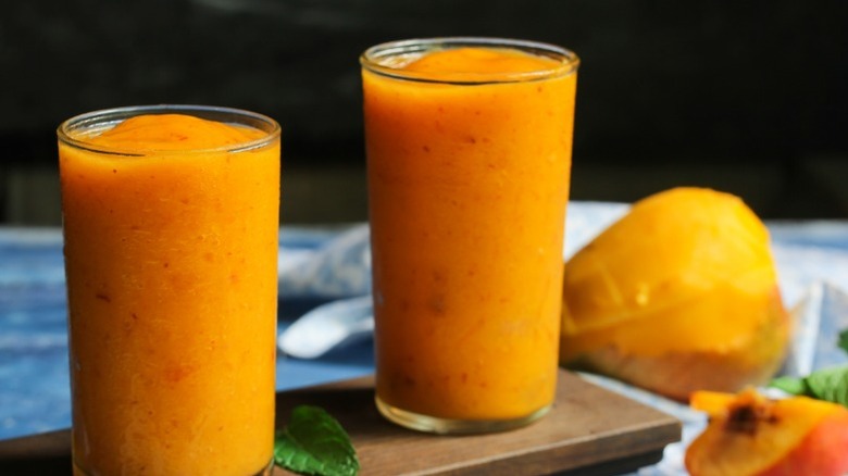 Two glasses of freshly made slushy cocktails with cut mango and other fruit on the side.