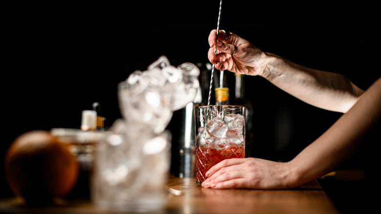 A bartender stirs a cocktail with a long spoon.