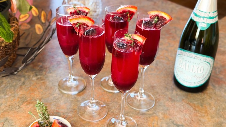 Mixed berry blood orange mimosas on countertop with Cava bottle