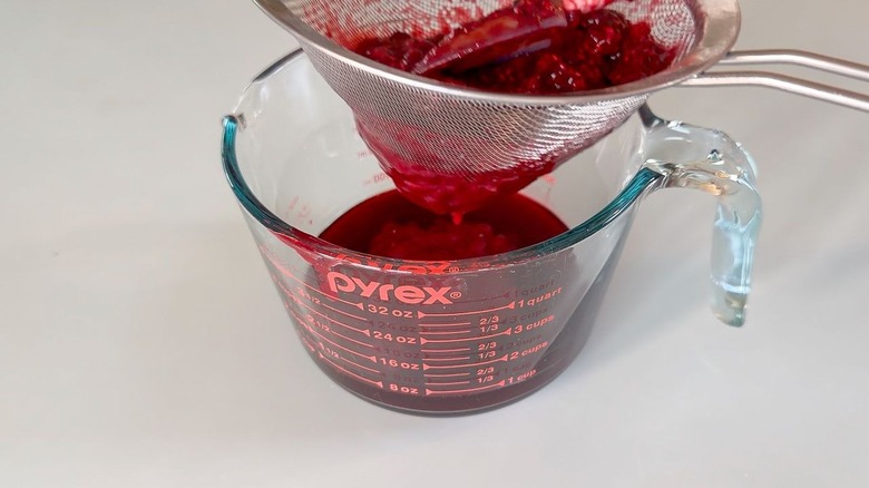 Straining mixed berry syrup through mesh strainer into pyrex measuring container