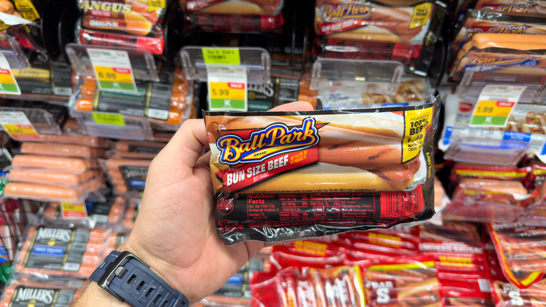 A customer holding a package of Ball Park hot dogs in the grocery store