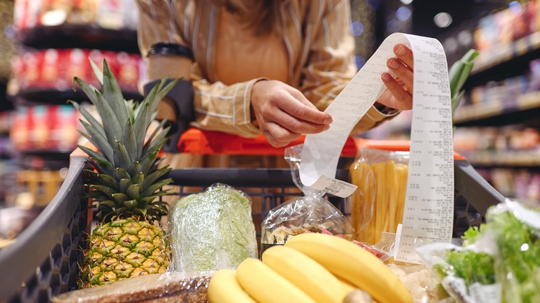Person holding long receipt over full grocery cart