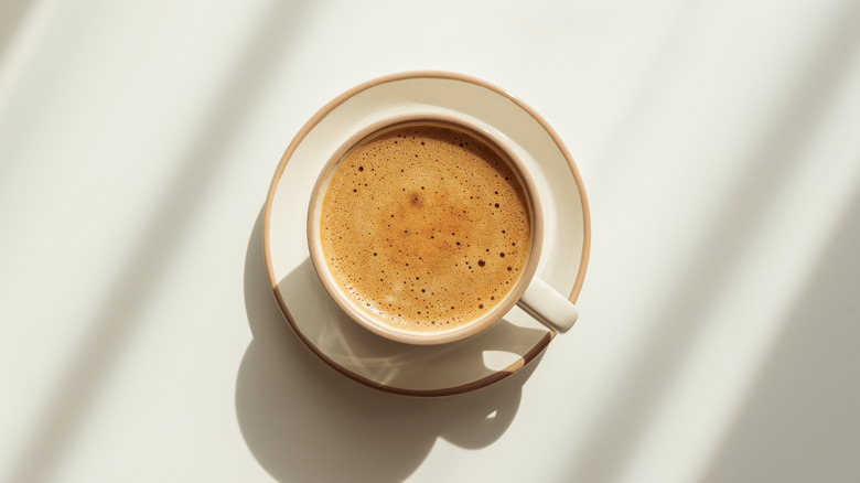 coffee cup with crema on light wooden table under sun light