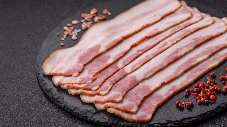 Slices of raw bacon on a black plate