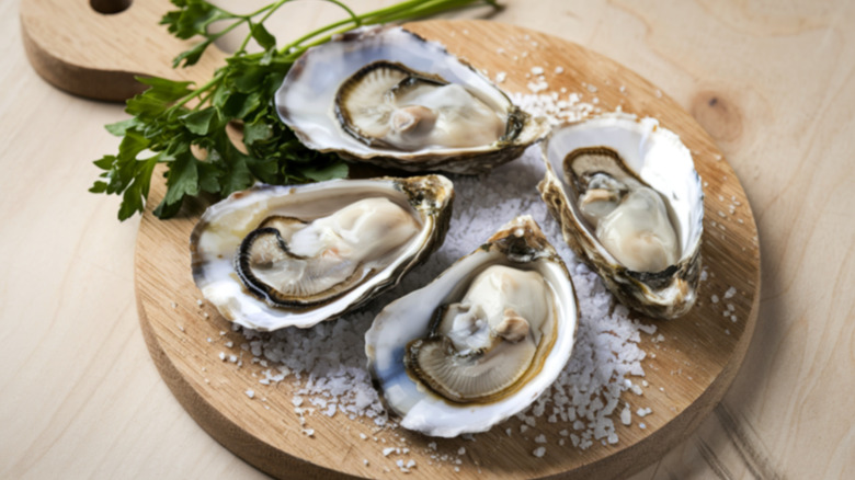 Four fresh oysters served on a wooden circular board.