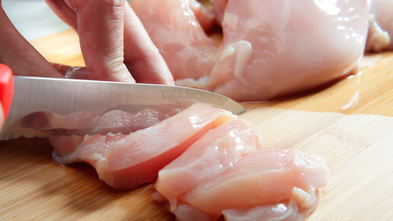 A hand without gloves chopping raw chicken.