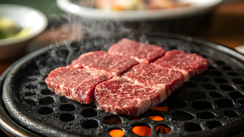 Marbled Wagyu beef sizzling on a hot grill.
