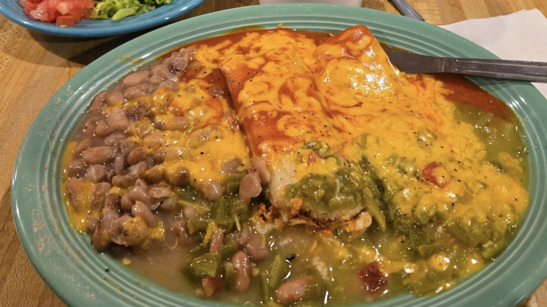 A green plate of enchiladas with melted cheese and green and red chile sauce, along with beans on the side