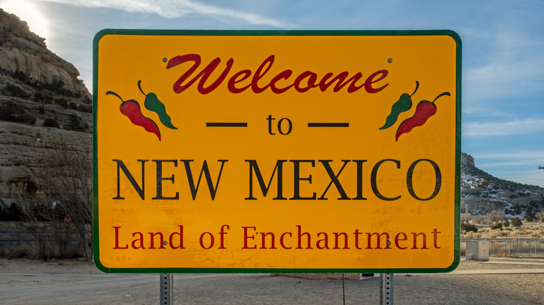 Yellow road sign stating "Welcome to New Mexico, Land of Enchantment" with red and green chiles around text