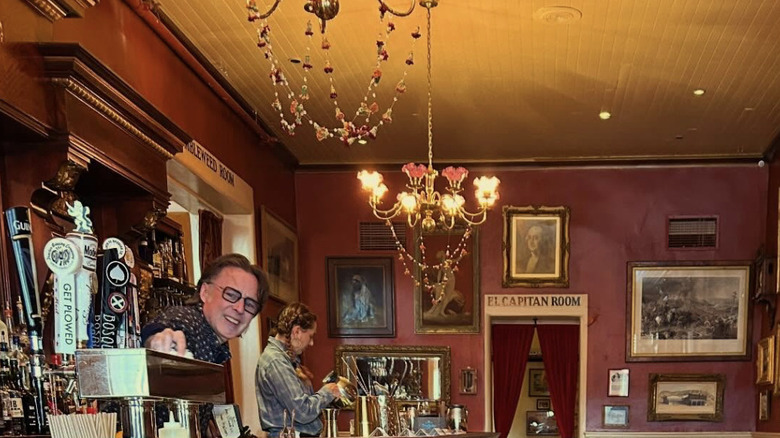 An Old West-style bar with red walls, chandelieres, and black-and-white photos on the walls
