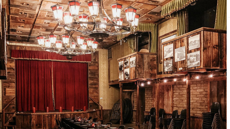 an 1800s opera house with a red-curtained stage, ornate chandeliers, and second-story opera boxes
