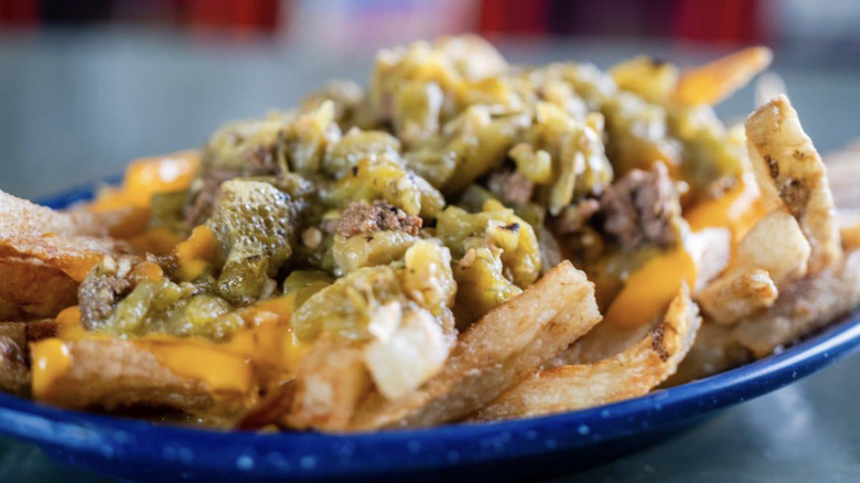 A blue plate covered with french fries smothered in melted cheese and chopped green chiles