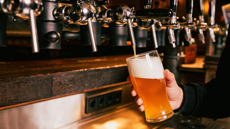 A man holding a pint of beer next to a tap