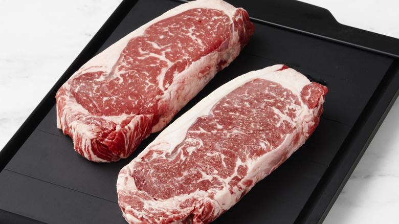 Two raw NY strip steaks on an aluminum thawing tray
